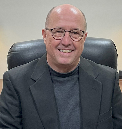 Photo of David Ivey smiling and sitting in desk chair wearing dark suit jacket