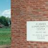 Granite cornerstone embedded in brick facade engraved with "Alabama Supercomputer Center Erected 1987 The State of Alabama Governor Guy Hunt" with old weathered barn in a green pasture in the background 